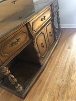 Angle side view showing carved wooden details, open shelving, and the lower cabinet doors with decorative handles.