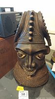 Full frontal image of the wooden tribal bust showing entire face and headdress positioned on a table next to a radio.