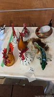 Collection of colorful hand-blown glass roosters and fish grouped on a table, showing vibrant colors and designs.