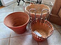 Photo showing three different woven baskets next to a metal rack on a tiled floor