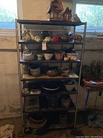 Full view of metal shelving with birdhouses on top and multiple planters, bowls, and garden decor items on shelves