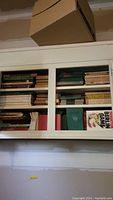 Shelf containing assorted hardback and paperback books, including a visible title 'Berlin Game' and some green hardcover books, various thicknesses and colors.