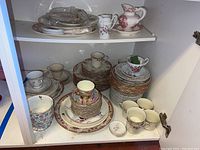 Multiple shelves with stacked plates, cups, saucers, pitchers and platters showing various floral and decorative patterns.