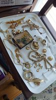 Full view of assorted costume jewelry pieces on white tray including necklaces, earrings, brooches and pendants