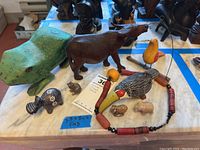 Photo showing the green wooden frog, brown wooden hippo, pottery bird whistle, stone animals, and beaded necklace displayed on a table.