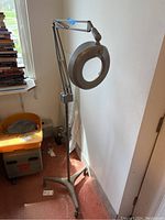 Full view of the lighted magnifier on adjustable stand showing height and base with four caster wheels.
