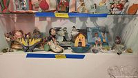 Shelved wooden art showing various painted and mixed media wooden figurines including a butterfly and dolls.