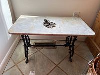 Full side view of rectangular marble top table with cast iron legs, showing surface wear and tear.