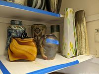 Photo shows the full group of seven vases on a shelf including variety of styles and colors as described.