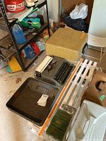 Vintage Hermes 4 typewriter with fitted case and three boxes of Singer ink ribbon on table in garage.