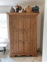 Front view of cabinet with closed paneled doors and decorative items on top, on tiled floor