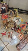Photo of assorted religious wood decor plaques, metal mobile with flying pieces, and various small ornaments including wooden hand and crosses, laid on tile floor.