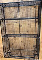 Front view of the black metal wire mesh 3 tier wall mount storage rack against wooden background showing the entire structure, including the bottom rack