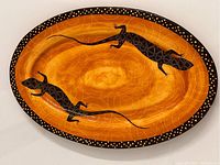 Full view of the oval ceramic tray showing the orange background with two black geometric patterned lizards and dotted black rim.