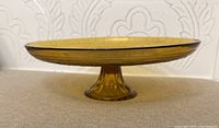 Side view showing the pedestal base and amber glass color with patterned details around edge.