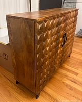 Side angle of brown wooden cabinet showing carved geometric front and flat natural wood finished side panel.