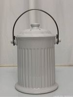 Front view of white ceramic countertop composter with metal handle raised and lid secured on top.
