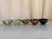 Set of five ceramic rice bowls lined up showing their varied glazing and colors
