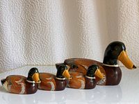 Side view of four hand-painted wooden duck figurines arranged from largest to smallest on a white surface with a textured white fabric backdrop.