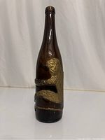 Front view of the brown glass bottle with gold monkey figure wrapped around it.