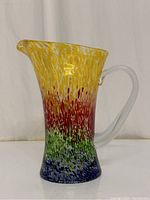 Side view of colorful hand blown glass pitcher with clear handle and spout.