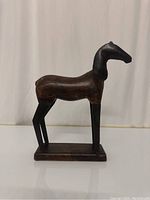 Front view of horse statue showing wooden body and metal legs and head on rectangular wooden base