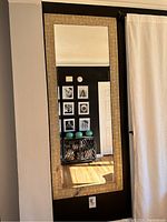 Full front view of large rectangular wall mirror mounted on black wall. Beige textured frame and clear reflective surface visible. Small wax marks on bottom edge of frame.