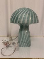 Mushroom-shaped glass table lamp shown unlit with its clear electrical cord and switch visible, displaying vertical green and white stripes.