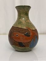 Front and side perspective of small pottery vase showing fish engraving with green and brown glaze finish.