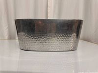 Front view of the oval stainless steel beverage tub showing hammered texture at bottom half and polished smooth rim on top.