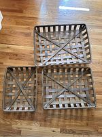Three wooden tobacco baskets arranged on floor, showing woven slat design with cross beams, varying sizes.