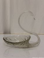 Side angle photo showing clear glass swan figurine with long curved neck and textured body forming a hollow bowl