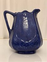 Front view of blue ceramic milk jug showing handle and spout, with embossed detailing near base.