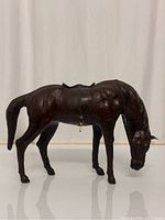 Front-side view of dark brown leather wrapped horse statue with saddle and bridle