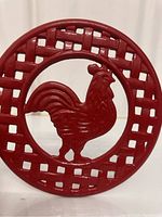 Front view of red cast iron trivet with rooster silhouette and lattice design.