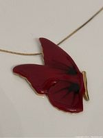 Close-up image of the red butterfly pendant showing the black wing details and gold edges on a thin chain.