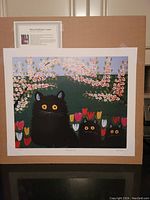 Full view of the lithograph print '3 Black Cats' by Maud Lewis showing three black cats with yellow eyes among tulips and blossoming branches.