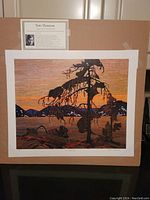 Full view of the lithograph print showing the artwork and accompanying information card about Tom Thomson taped above it.