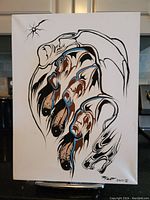 Front view of the original painting showing abstract bear paw design in black, brown, and blue on white stretched canvas.