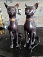 Pair of solid bronze cat sculptures on black countertop, showing front and side views of both pieces.