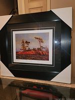 Angled view of the professionally framed print with black frame and corner protectors showing the artwork and part of the framing.