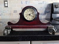 Front view of small cherry wood mantle clock showing clock face with Roman numerals and decorative metal feet.