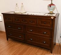 Front view of the 7-drawer wooden dresser showing four small top drawers with round black knobs and three larger drawers with oval handles, sitting on a wood floor.