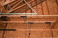 Wide view of the pulley system mounted on wood 2x4 boards attached to ceiling rafters in a garage-like environment.