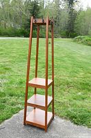 Full view of a tall wooden hall tree with three shelves and eight coat hooks, placed outdoors on concrete with grass background.