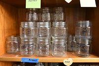32 clear glass Kerr jars arranged on wooden shelves, showing the front embossed branding on the glass.