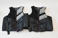 Two HyperLite men's extra-large life jackets laid flat, showing front zipper, multiple straps and padded design in black and gray with red trim.