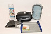 Image showing all items in the lot including HP Officejet 5255 printer, shelf liner rolls, display case, paper cutter, desk organizers, humidity monitor, and wall straps.