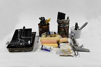 Full view of painting supplies including paint brushes in containers, rollers, scrapers, and paint tubes grouped together.