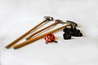 Two sledge hammers and one axe with wooden handles, arranged side by side alongside black nylon straps and an orange tie-down strap